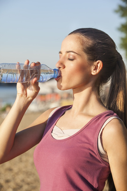 Мила молода жінка п'є воду після вправ на відкритому повітрі
 - Фото, зображення