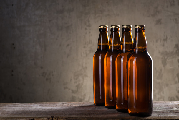Свіжозварені пляшки пива поспіль над сірою бетонною стіною
 - Фото, зображення