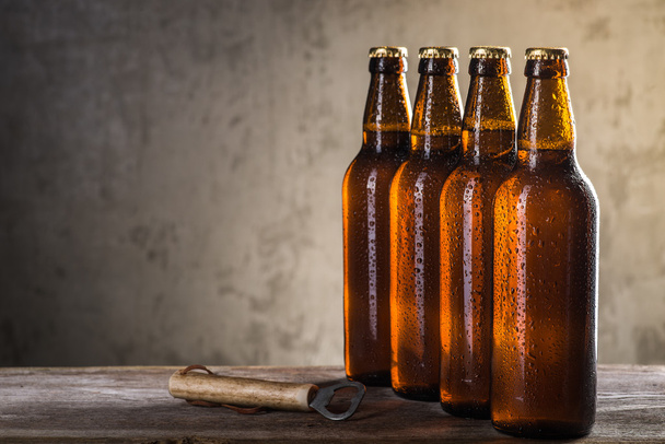 Świeżo parzonej butelek piwa z rzędu z otwieraczem do butelek w szary mur beton - Zdjęcie, obraz