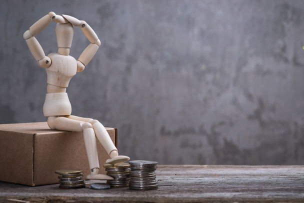 Small wooden dummy with sitting with coins over the grey concrete wall - Photo, Image