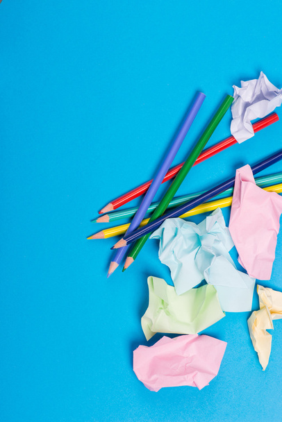 Several color pencils with crumpled color paper over the blue background - Photo, image