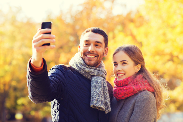 smiling couple with smartphone in autumn park - Fotoğraf, Görsel