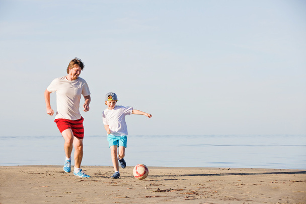 Feliz padre e hijo juegan fútbol o fútbol en la playa
 - Foto, Imagen