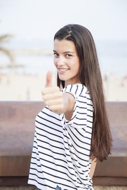 Портрет девушки, показывающей большой палец и смотрящей в камеру
 - Фото, изображение