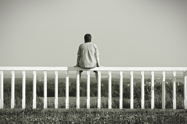 Mann sitzt auf einem Zaun mit Blick auf die Landschaft - Foto, Bild