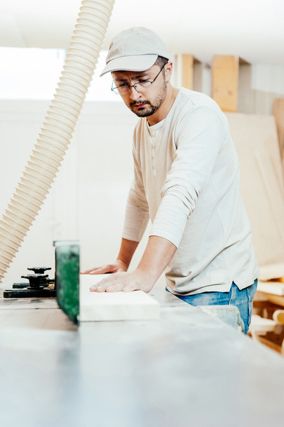 Carpintero trabajando cortando algunas tablas, lleva gafas de seguridad y protección auditiva
 - Foto, Imagen