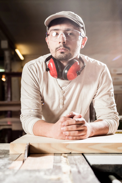 Carpintero trabajando con herramienta industrial en fábrica de madera con gafas de seguridad y protección auditiva
. - Foto, imagen