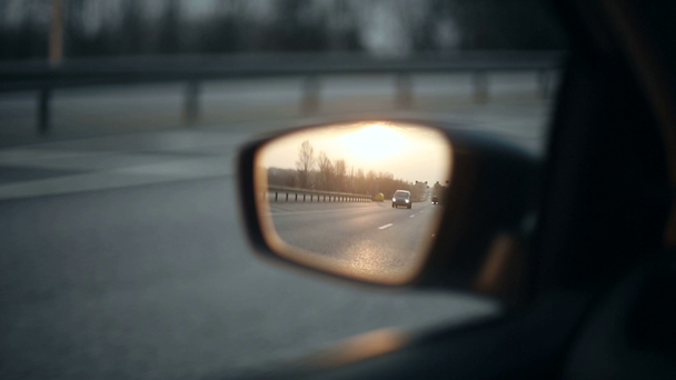 Zicht op de weg in de rearview spiegel van een auto bij zonsondergang - Video
