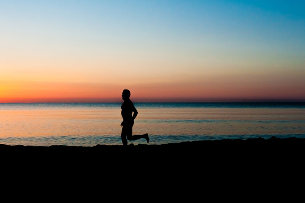 Silhouet van het runnen van man op het strand bij zonsopgang - Foto, afbeelding