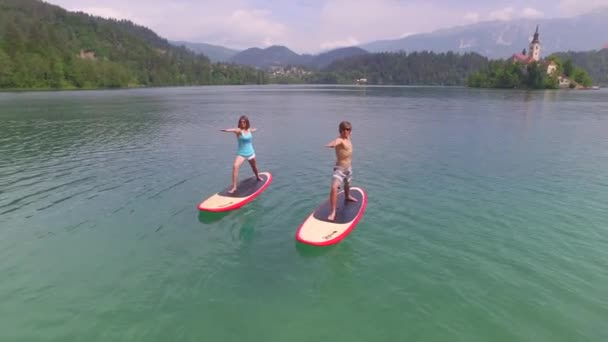 AERIAL: Flying around young couple doing yoga on SUP boards - Footage, Video