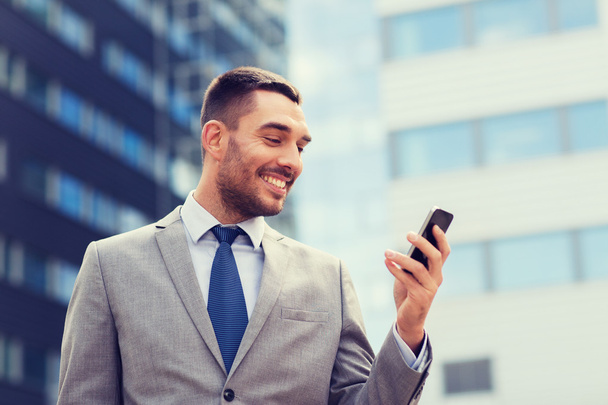 smiling businessman with smartphone outdoors - 写真・画像