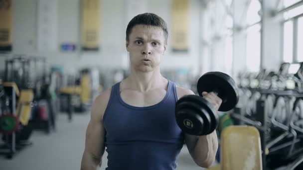 Man bodybuilder execute exercise with dumbbells in gym. Full face shot - Footage, Video
