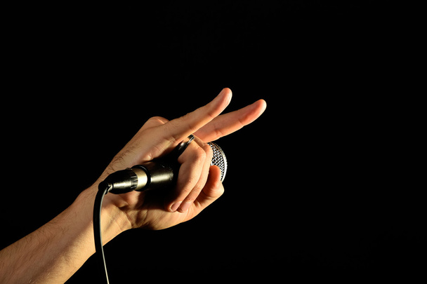 Χέρι με το μικρόφωνο και το διάβολο κέρατα που απομονώνονται σε μαύρο - Φωτογραφία, εικόνα