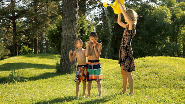 Äiti kaataa vettä kastelukannusta onnellisille lapsille vihreässä puistossa
. - Materiaali, video