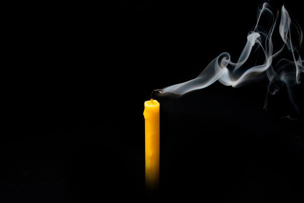extinguished candle yellow with smoke, isolated over black. - Photo, Image