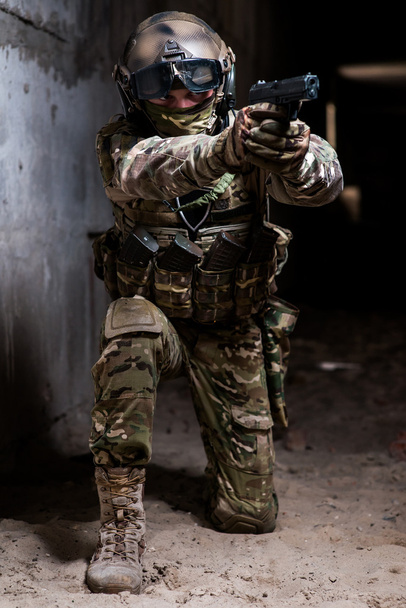 Gewapende man in militaire camouflage gericht zijn pistool op knieën - Foto, afbeelding