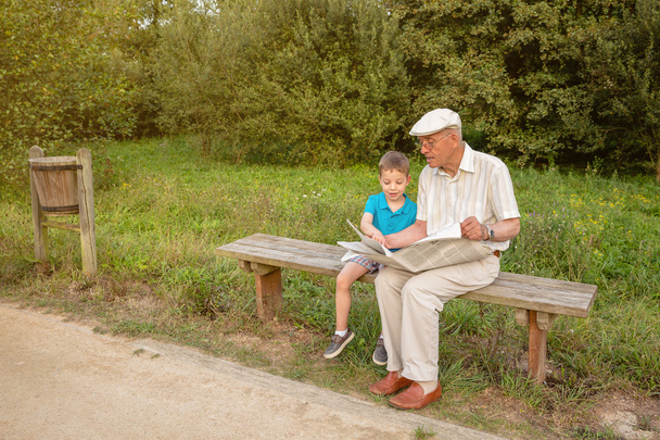 Старший мужчина и ребенок читают газету на улице
 - Фото, изображение