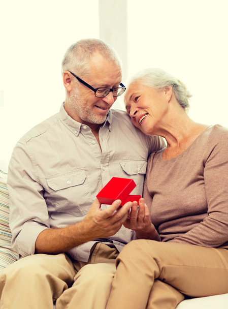 feliz pareja de ancianos con caja de regalo roja en casa
 - Foto, Imagen