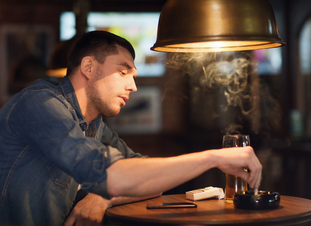 man drinking beer and smoking cigarette at bar - Fotoğraf, Görsel
