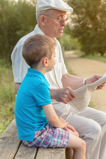 Senior man and child reading a newspaper outdoors - Photo, Image