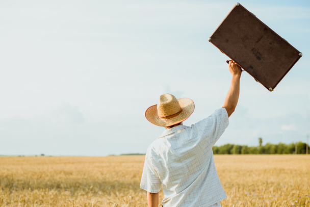 Man in straw hat  tossing up a retro suitcase - Zdjęcie, obraz