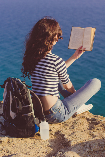 Girl traveler is sitting on mounrain peak and reading book - Foto, Imagem