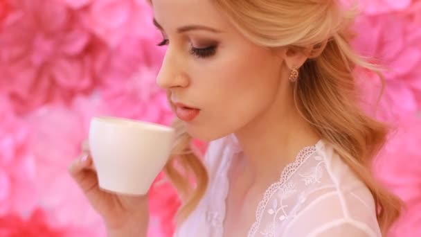 ピンクの花の背景に白のカップから飲む若い美しい花嫁 - 映像、動画