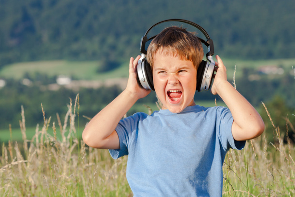 Cute 6 year old boy listening to music on headphones in nature - Photo, Image