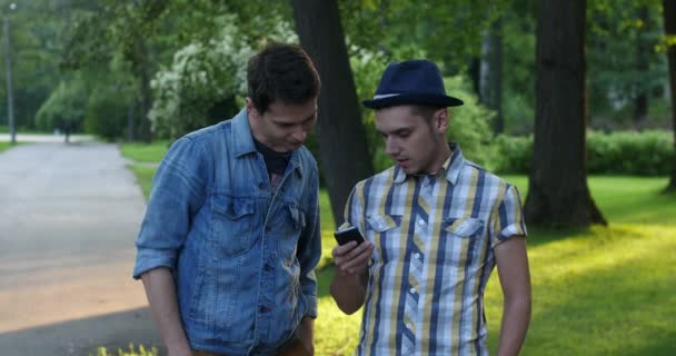 Im Park trafen sich zwei Freunde. Sie besprechen die Bilder am Telefon. - Filmmaterial, Video