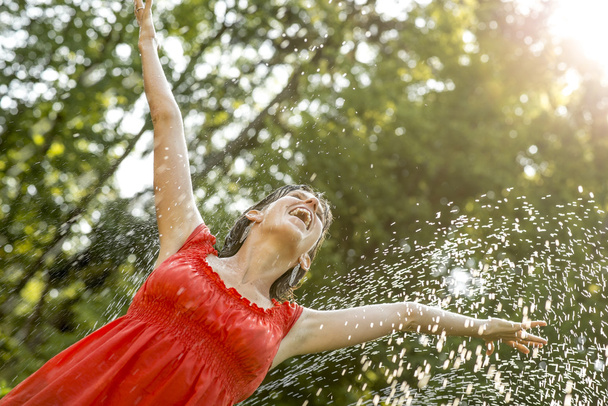 Счастливая молодая женщина, стоящая под брызгами воды на горячем сумме
 - Фото, изображение
