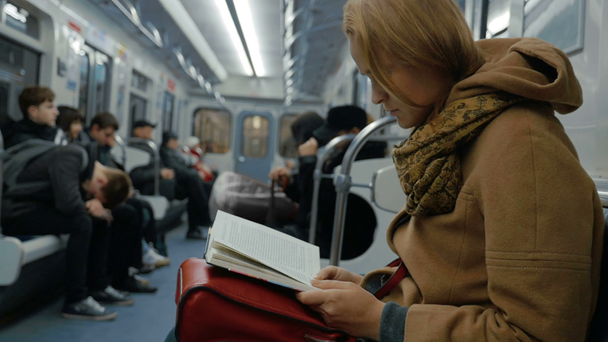 νεαρή γυναίκα διαβάζοντας ένα βιβλίο στο μετρό - Πλάνα, βίντεο