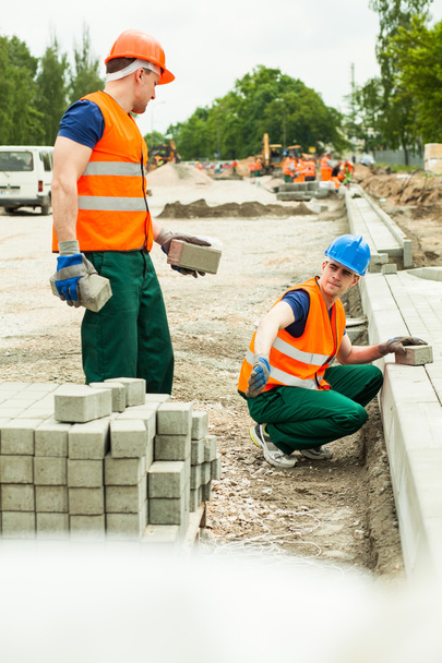 Trabalhadores da construção civil que instalam pedras de pavimentação
 - Foto, Imagem