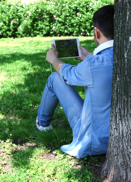 Man with headphones resting under tree in park - Foto, imagen