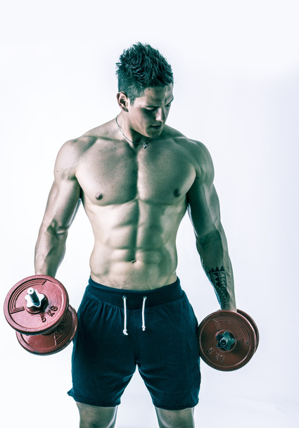Muscular shirtless young man exercising biceps with dumbbells - Zdjęcie, obraz