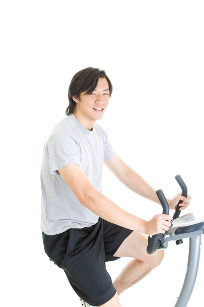 Joven asiático hombre montar bicicleta de ejercicio aislado en blanco backgroun
 - Foto, imagen