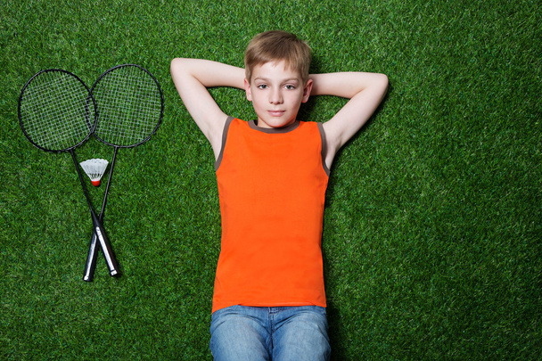 Boy lying with badminton racket on green grass - Foto, Imagen