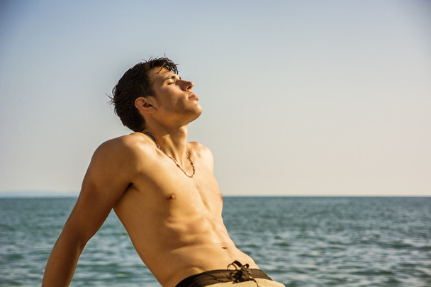 Smiling young man sitting by sea or ocean shore sunbathing - Φωτογραφία, εικόνα