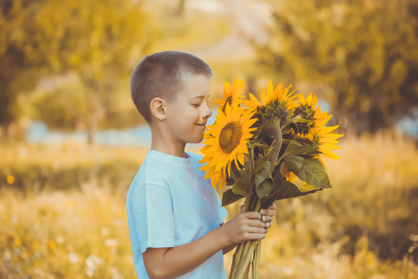 Onnellinen poika kukkakimpun kanssa kesäkenttää vastaan
 - Valokuva, kuva