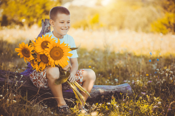 Gelukkige jongen met boeket van zonnebloemen tegen zomer veld - Foto, afbeelding