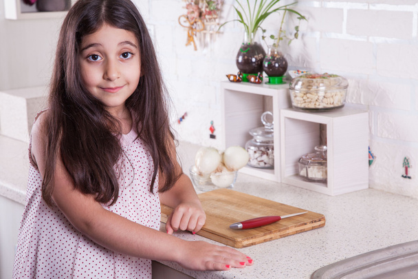 Beautiful little middle eastern 7 years old girl is working with knife and onion in the white kitchen. - Foto, Bild