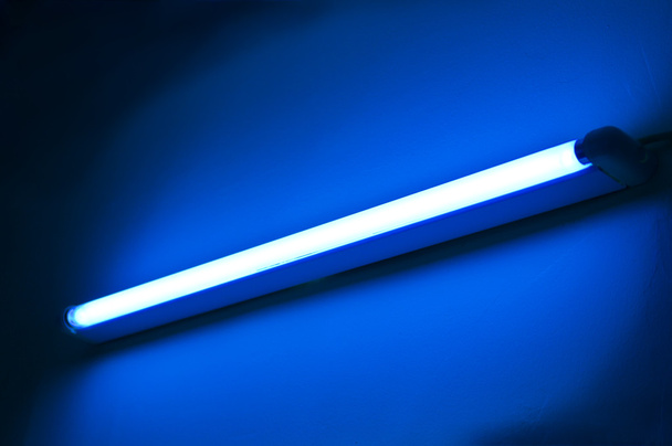 Lâmpada fluorescente brilhando na parede de cor azul
 - Foto, Imagem