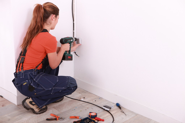 Woman drilling hole in wall - Foto, afbeelding