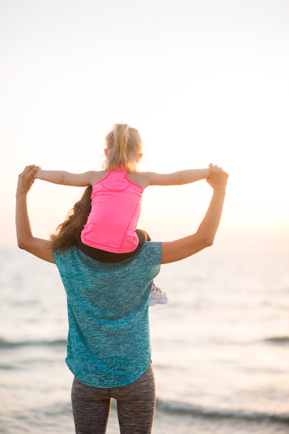 Mother holding young daughter on shoulders at sunset on beach - Foto, Imagen