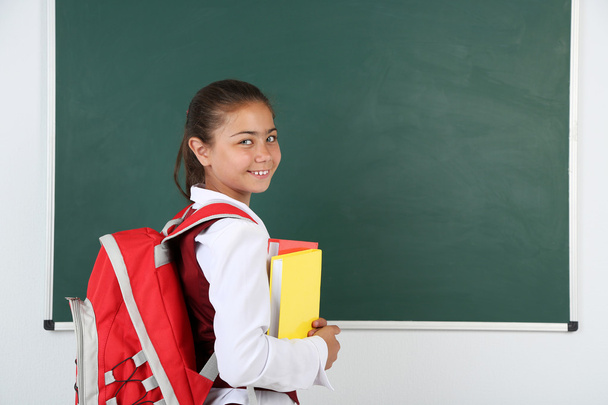 Beautiful little girl standing near blackboard in classroom - Foto, Imagen