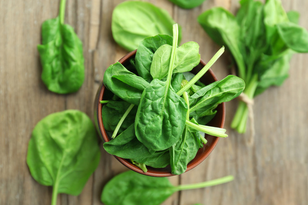 Bowl of fresh spinach leaves on wooden table, closeup - Фото, зображення