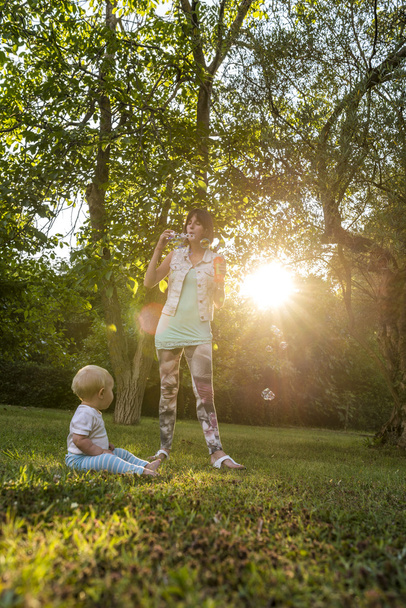 fröhliche junge Mutter pustet Seifenblasen in Richtung ihres kleinen Jungen - Foto, Bild