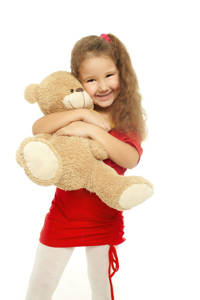 Little smiling girl is hugging with bear in red dress - Photo, Image