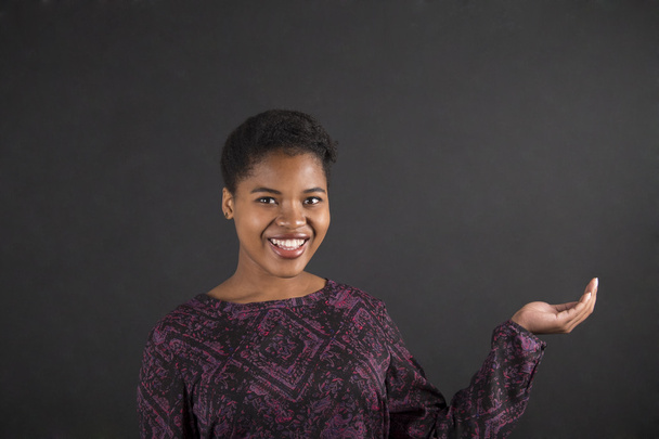 African woman holding hand out on blackboard background - Foto, immagini