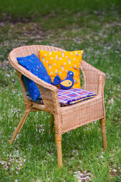 Wicker chair with cushions and a plaid close-up on background of grass in the garden. - Foto, Imagen