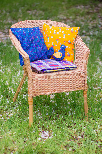 Wicker chair with cushions and a plaid close-up on background of grass in the garden. - Fotó, kép